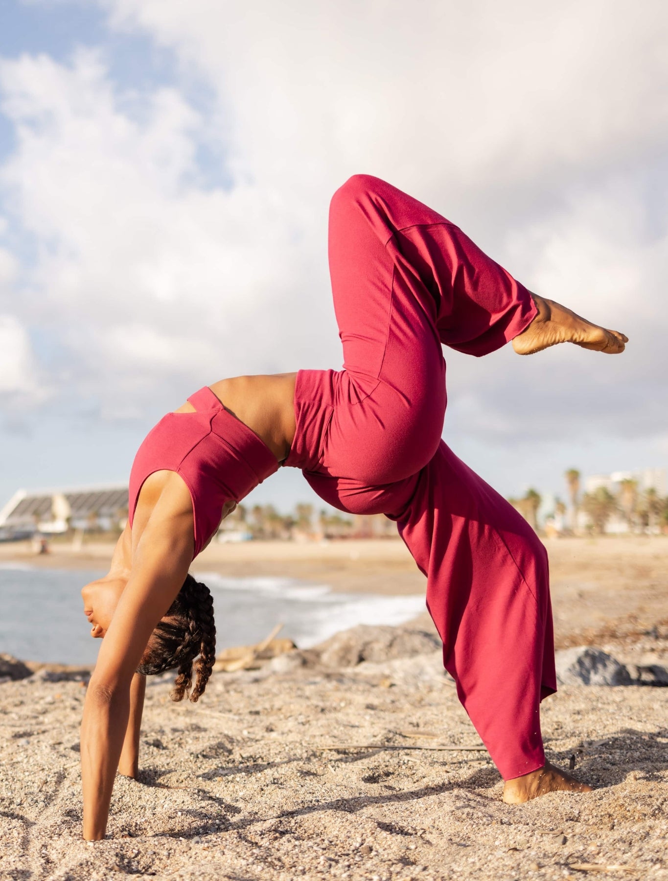 Shambhala Yoga's embodiment of strength and grace - a practitioner performs an advanced asana on the beach, wearing sustainable plum-colored yoga wear, exemplifying the balance between human agility and the natural world.